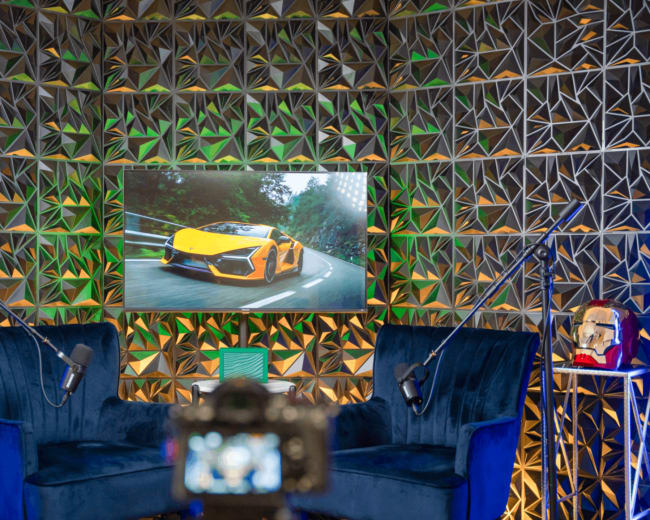 A modern studio setup features two blue chairs and a large screen displaying a yellow sports car against a geometric, colorful backdrop.