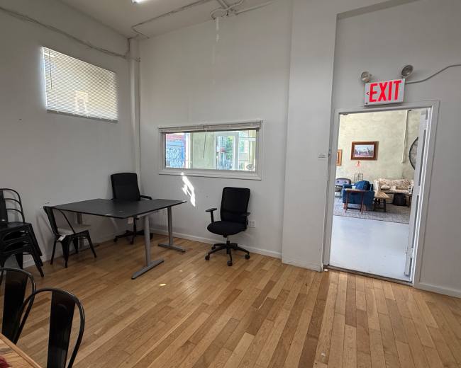 The image shows a bright, empty room with a table and chairs on one side and a doorway leading to another area on the right.