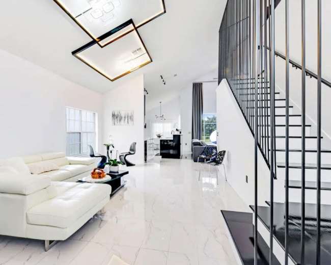A modern interior living space with a white sectional sofa, a sleek dining area, and a staircase leading to an upper level.