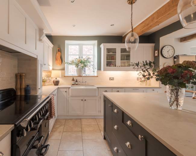 A modern kitchen features white cabinetry, a large island with a gray base, a black stove, and a farmhouse sink, with natural light illuminating the space.