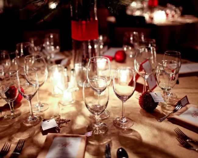 A elegantly set dining table features multiple glasses, red decorations, and menu cards under soft lighting.