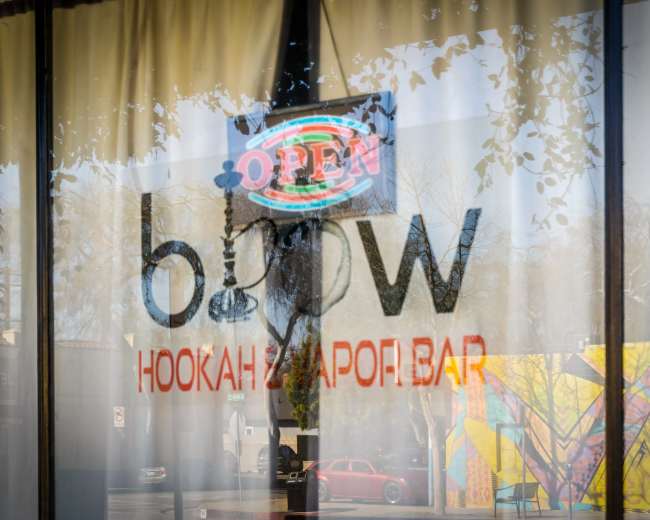 A storefront window reflecting an "OPEN" neon sign and the name "blow" along with the words "HOOKAH & VAPOR BAR."
