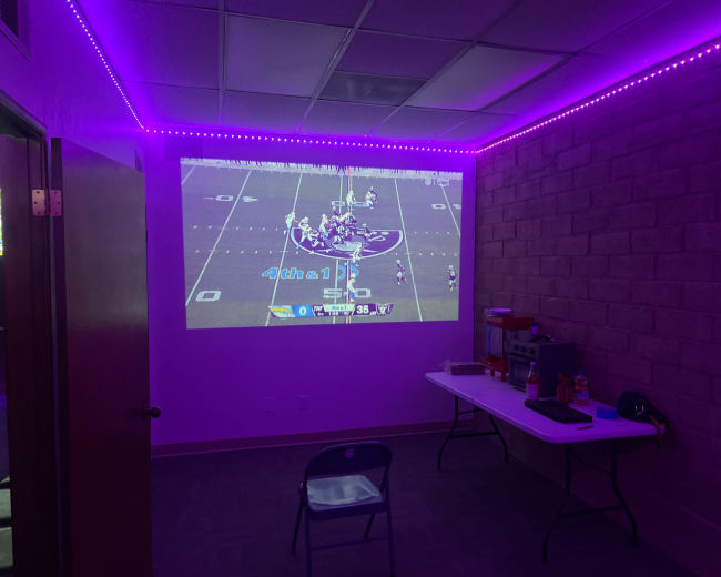 A football game is projected on a wall in a dimly lit room with purple LED lights.