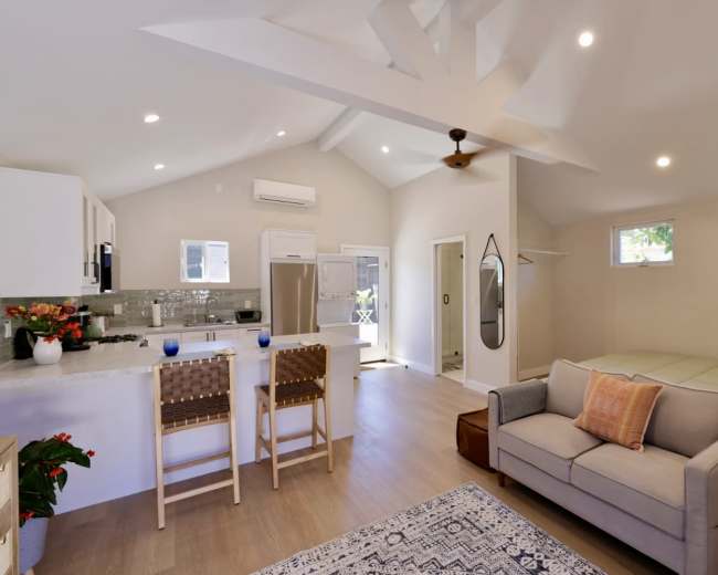 A modern, open-concept living space with a kitchen, a seating area, and a bedroom area featuring a large window and sliding doors.