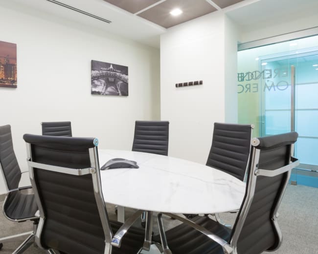 A modern conference room features a round marble table surrounded by black leather chairs and glass walls.