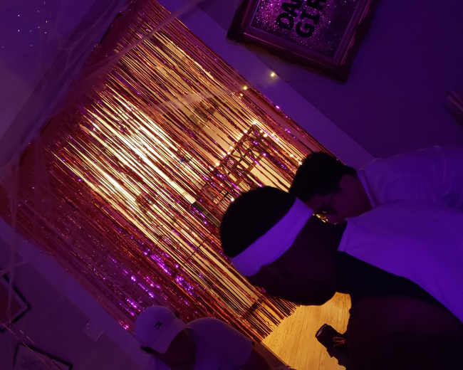 People are seated in a dimly lit room with a shimmering, golden curtain backdrop.