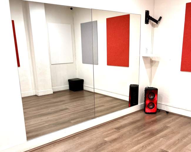 The image shows a dance studio with mirrored walls, a wooden floor, and two red wall panels.
