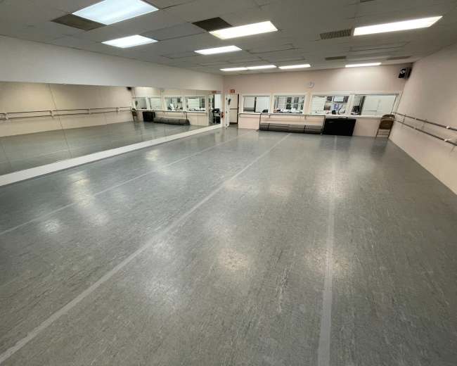 The image shows a spacious dance studio with mirrored walls, wooden ballet bars, and a polished gray floor.