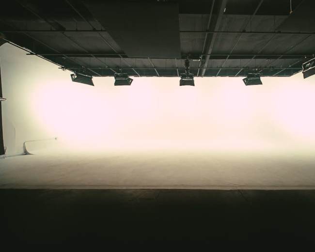 An empty studio space features a seamless white backdrop and overhead lighting.