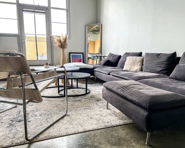 A modern living room features a gray sectional sofa, a round coffee table, a chair, and a large mirror against a light green wall.