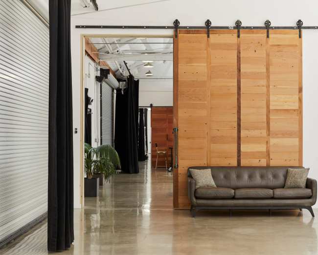 The image shows a modern interior space featuring a brown leather sofa and large wooden sliding doors on a minimalistic concrete floor.
