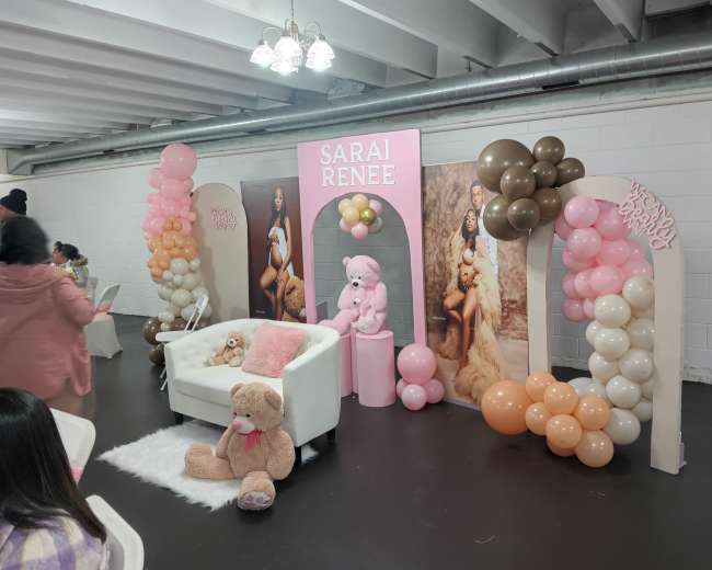A decorated event space featuring a plush white couch, balloon arches in various colors, and themed backdrops displaying "Sarai Renee."