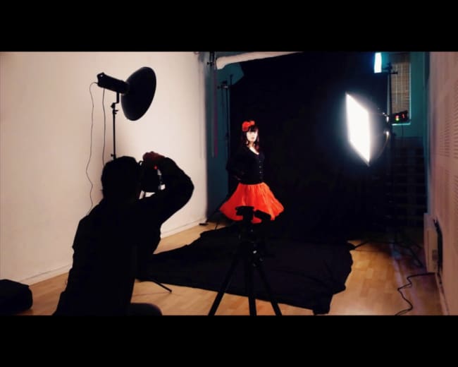 A photographer captures a portrait of a child in a red dress against a black backdrop in a studio setting.