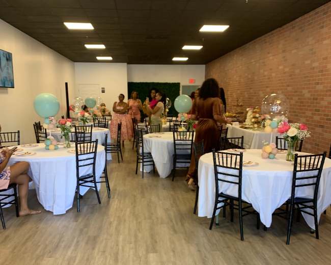 A decorated event space with several tables set for a celebration, featuring floral centerpieces and balloons.