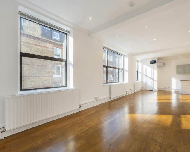 The image shows a spacious, well-lit room with hardwood flooring and large windows.