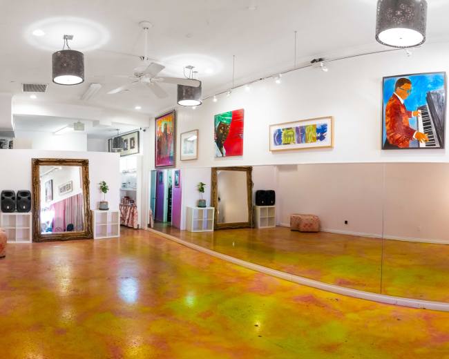 The image shows a brightly colored dance studio with a mirrored wall, vibrant floor, and several artworks displayed on the walls.