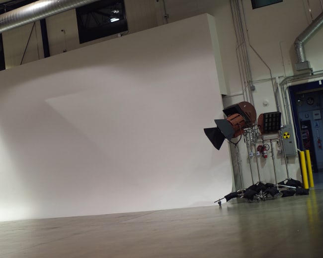 A large white backdrop is set up in an empty studio space, with soft lighting and a dark curtain on one side.