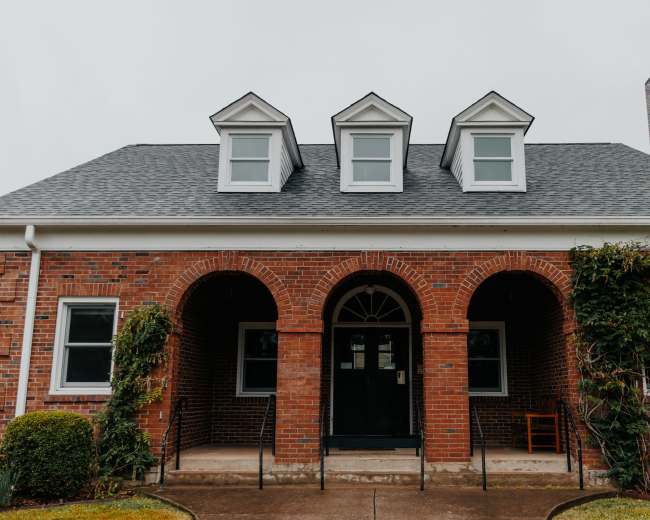 The image shows a brick house featuring a symmetrical facade with three gabled dormers and arched entrances on both sides.