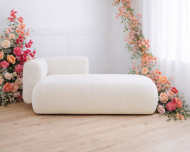 A minimalist room features a white sculptural sofa adjacent to a floral arrangement arching from the wall.
