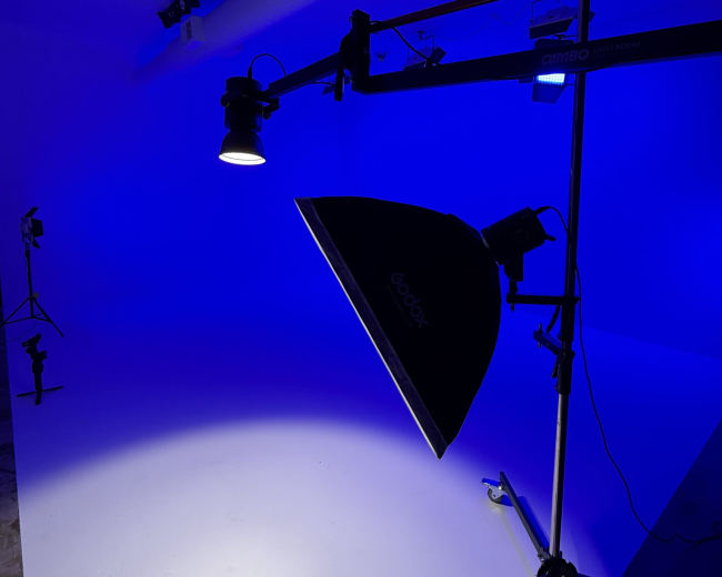 A lighting setup featuring a blue background with a softbox and additional light sources is positioned on a studio stand.