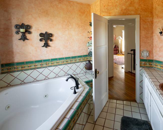The image shows a bathroom featuring a jetted bathtub, a decorative sink, and an open door leading to another room.