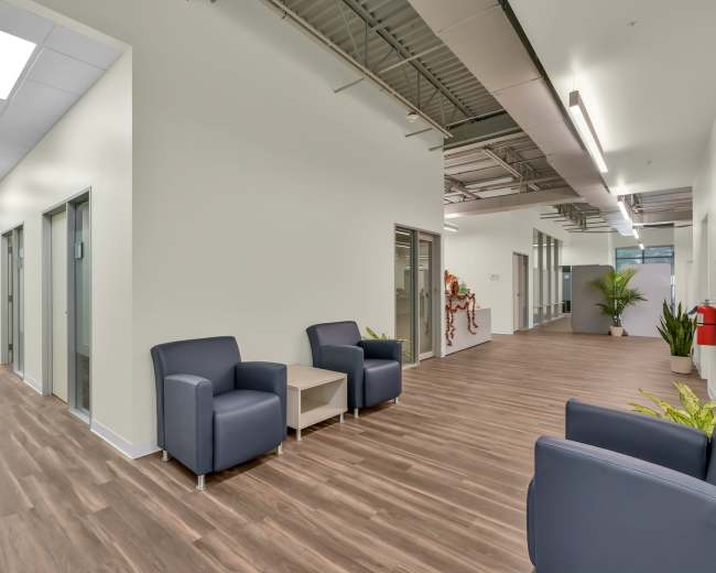 A modern office corridor with two seating areas and multiple closed office doors on either side.