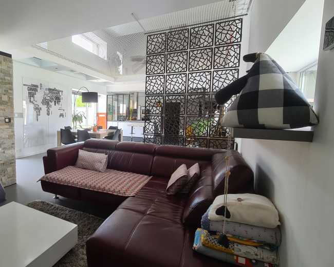 The image shows a modern living room with a maroon leather sofa, a stone-accent wall, and a glass partition leading to a dining area.