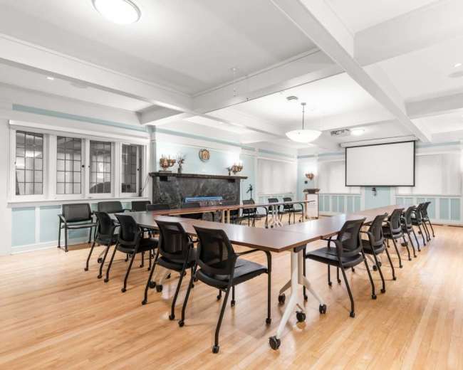 A spacious meeting room features multiple tables arranged for discussions, with black chairs and a large screen mounted on the wall.