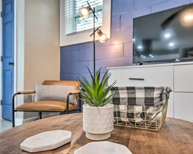 The image shows a modern living room setup featuring a plant on a wooden coffee table, a light fixture, a television, and a chair beside a blue wall.