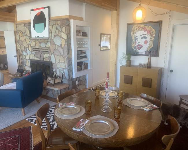 A spacious living room with modern furniture, large windows overlooking a snowy landscape, and exposed wooden beams on the ceiling.