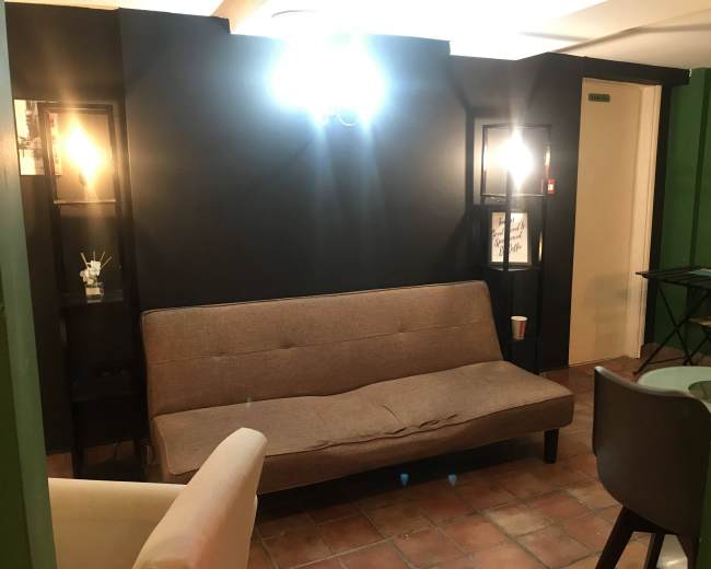 A small, cozy room featuring a brown sofa, two display shelves with lights, and a small table in the corner.