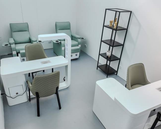 The image shows a minimalist salon interior with two green chairs, a black shelving unit, and two white workstations.