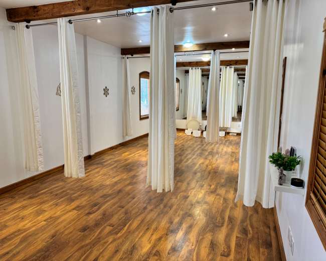 The image shows an empty studio space with wooden flooring, white walls, and several curtains dividing the area.