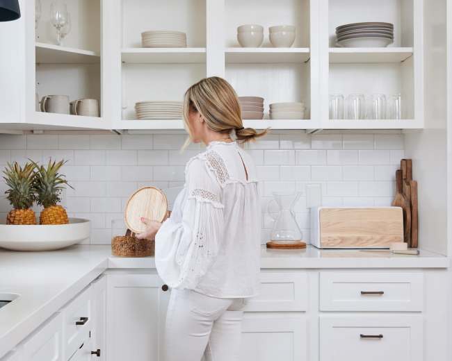 A person stands in a modern kitchen, inspecting items on a countertop next to an arrangement of pineapples.