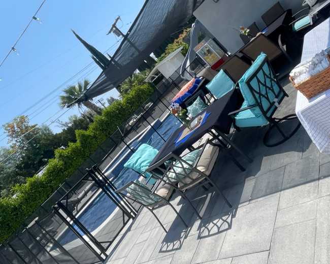 A patio area with outdoor furniture, a swimming pool, and a protective shade structure overhead.