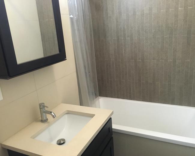 The image shows a bathroom featuring a light-colored tub, a modern sink with a faucet, and tiled walls in neutral tones.