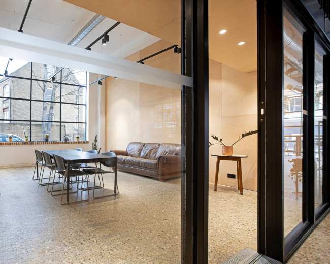 A modern, well-lit meeting space featuring a long table, chairs, a sofa, and large windows.