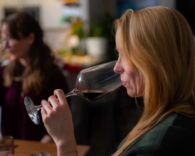 Two women are drinking wine from large glasses at a dinner table.