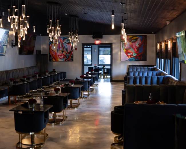 The image shows a modern restaurant interior featuring dark seating, sleek tables, abstract artwork on the walls, and pendant lighting.