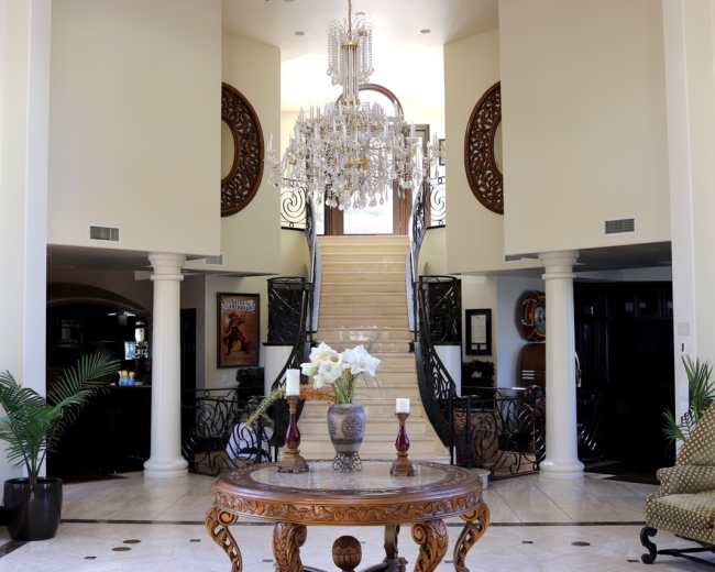 A grand foyer with a chandelier, a staircase, and a circular table adorned with flowers.