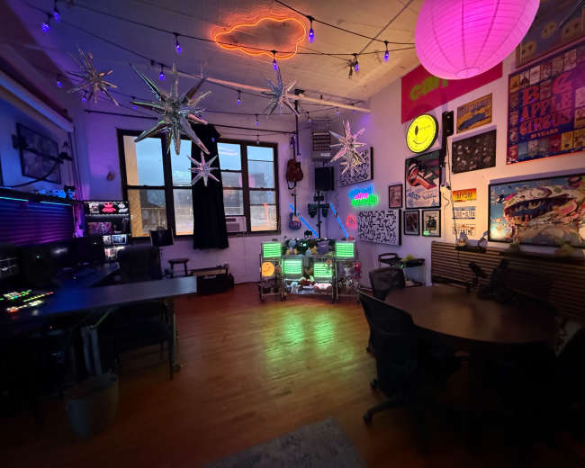 The image showcases a vibrant creative workspace featuring colorful lighting, decorations, and multiple computer stations.