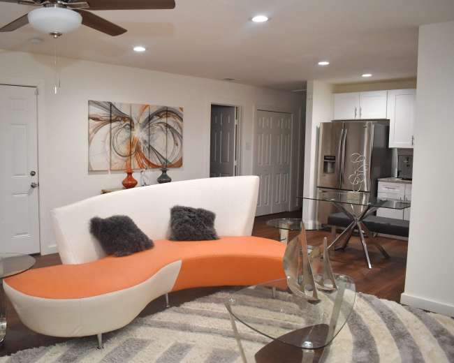 A modern living space features a curved orange and white sofa, glass tables, and a kitchen area in the background.