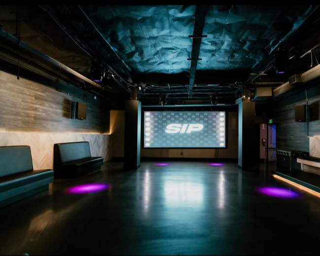 The image shows a spacious, modern event venue with a large screen displaying the word "SIP" and purple lighting on the floor.