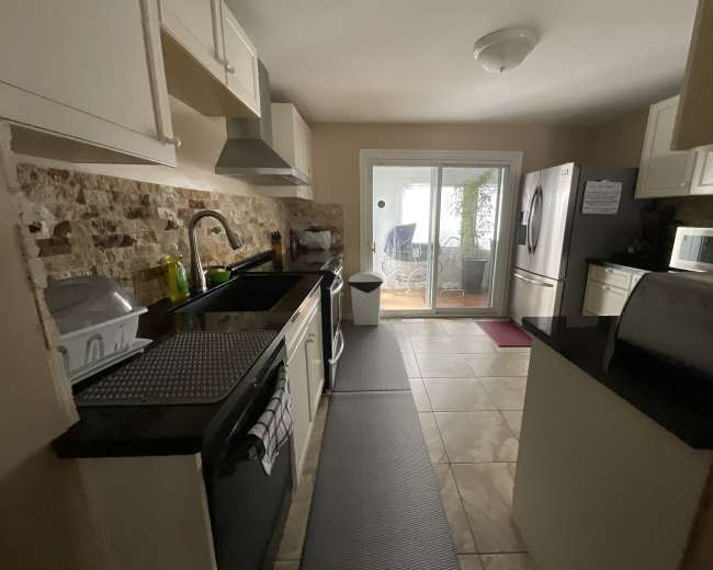 The image shows a kitchen with white cabinets, a black countertop, and stainless steel appliances, leading to a glass sliding door that opens to a porch area.