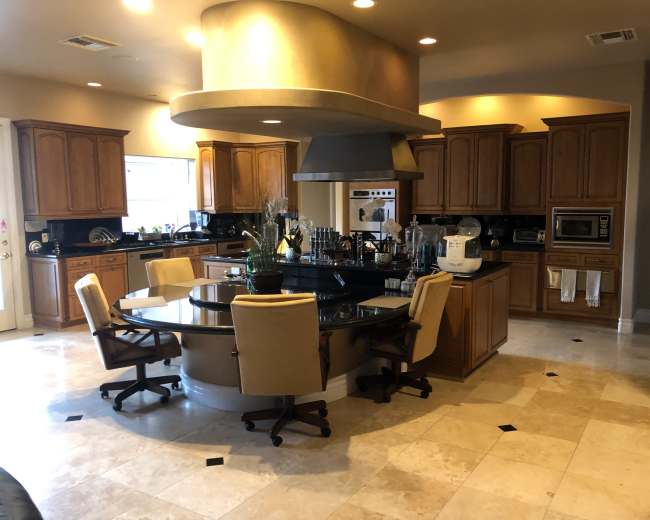 The image shows a spacious kitchen with wooden cabinets, a large island with seating, and modern appliances.