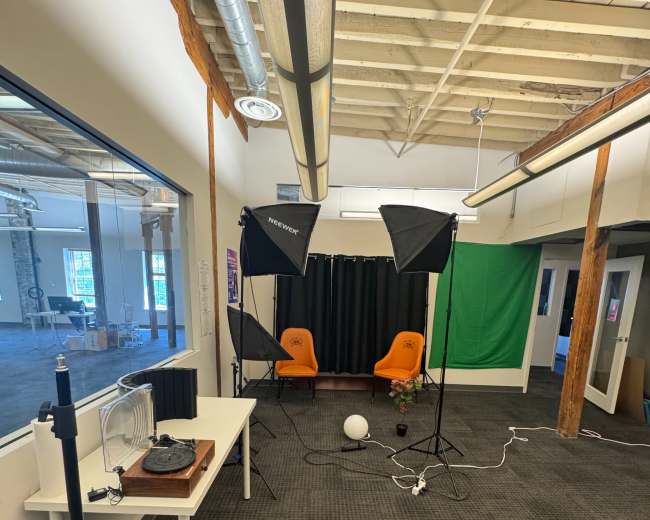 The image shows a well-lit photography studio setup with two orange chairs, softbox lights, and a green backdrop.