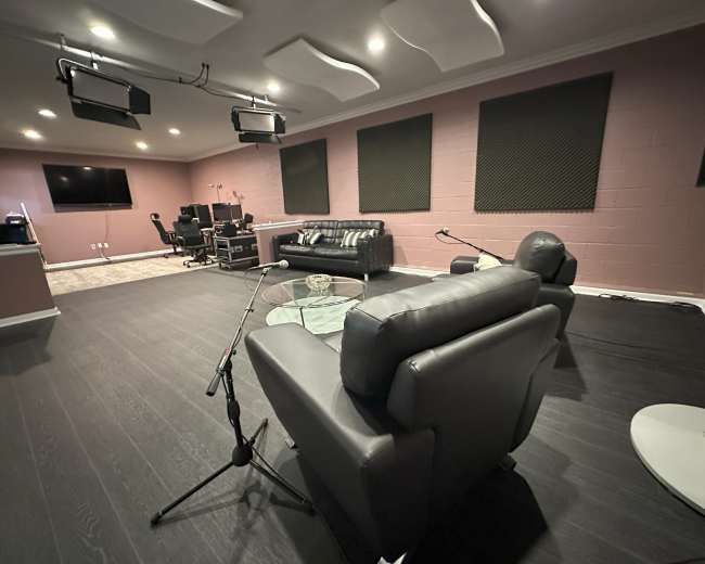 The image depicts a modern recording studio featuring black leather chairs, a glass table, and multiple workstations with audio equipment.