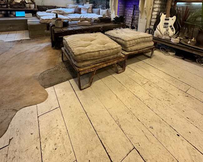 The image shows a cozy living room featuring a white-brick wall, a fireplace with purple lighting, several cushioned lounge areas, and decorative plants.