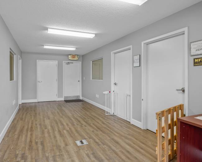 The image shows a narrow hallway with gray walls, a wooden floor, and several closed doors along one side.