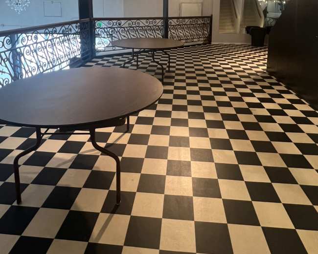 An indoor space featuring a checkered black and white floor with several round tables and decorative lighting overhead.